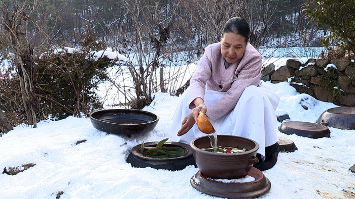 눈으로 덥힌 추운 겨울 장독대에서 김치를 꺼내고 있는 모습 (사진: 문화재청)