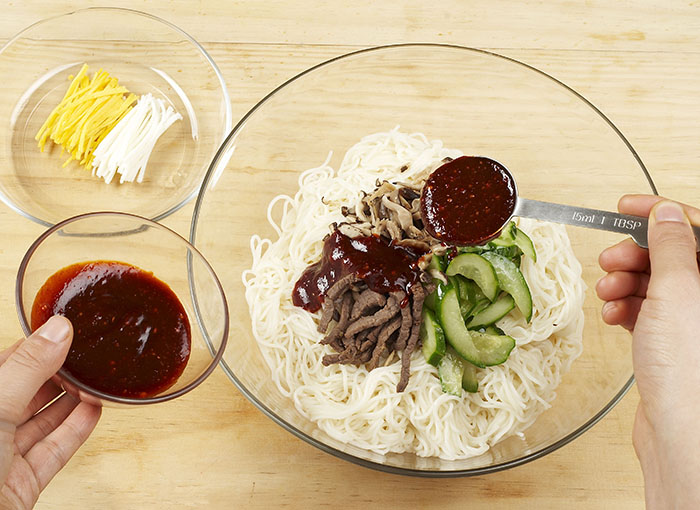 삶은 국수에 쇠고기와 표고버섯 등 고명과 양념장를 넣고 고루 버무린 뒤 황백지단을 고명으로 얹어 낸다.