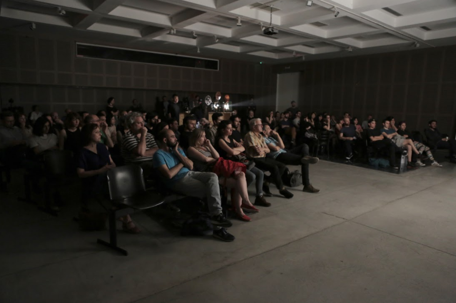 아르헨티나 관객들이 16mm 영사기 필름이 재현하는 한국의 역사적 자취를 담은 영상에 알란 코루티스의 즉흥 기타 연주를 감상하고 있다.