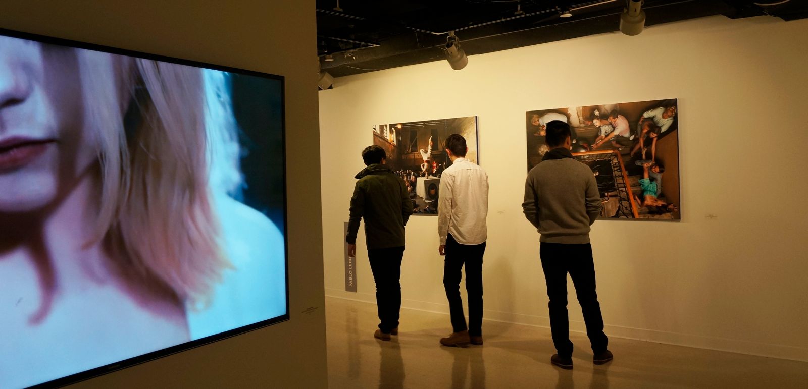 전시장 우측에 위치한 이동 벽에 클라라 욜디의 비디오 작품이 전시되어있으며, 그 뒤편에 전시되어있는 파블로 라라의 사진작품을 관람객들이 유심히 감상하고 있다.