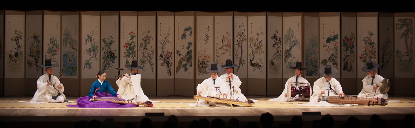 전통의상을 입고 무대에 앉아 아쟁, 거문고, 가야금, 피리, 단소, 징 등 다양한 전통 악기를 연주하는 국립국악원 단원들의 모습.