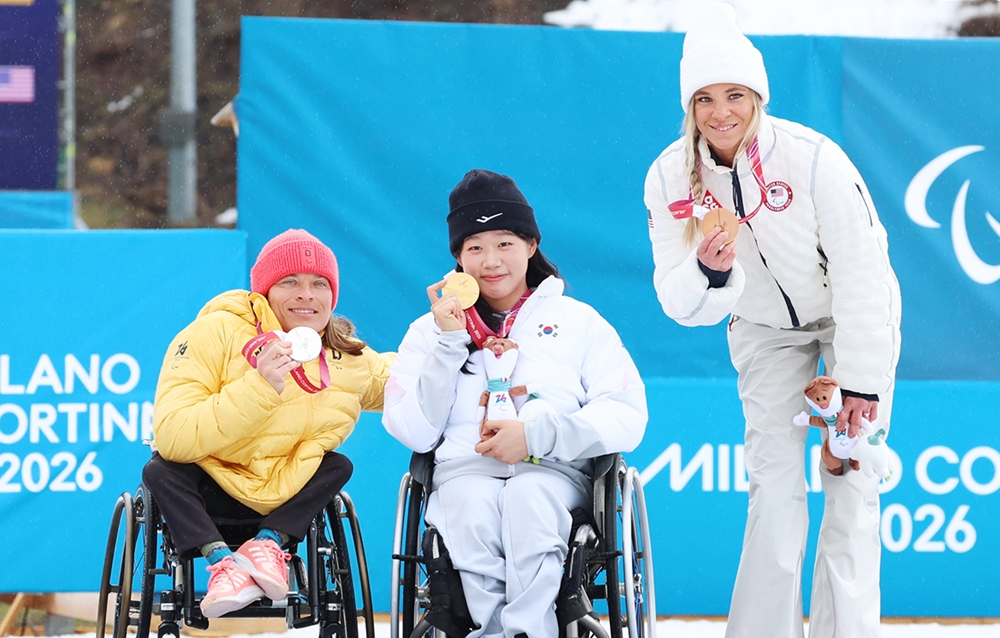 ▲ 김윤지(가운데)가 15일(현지 시간) 이탈리아 테세로 크로스컨트리 스타디움에서 열린 2026 밀라노-코르티나담페초 동계패럴림픽 크로스컨트리 스키 여자 20㎞ 인터벌 스타트 좌식 시상식에서 금메달을 목에 걸고 포즈를 취하고 있다. 